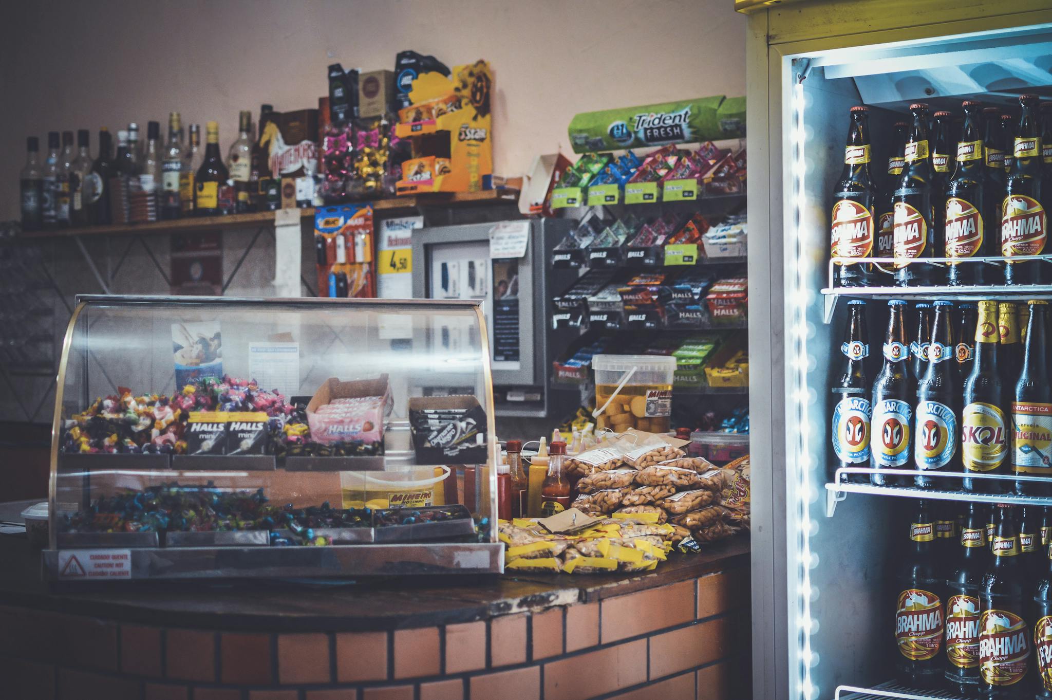 A well-stocked convenience store counter with snacks, drinks, and a refrigerator showcasing beverages.